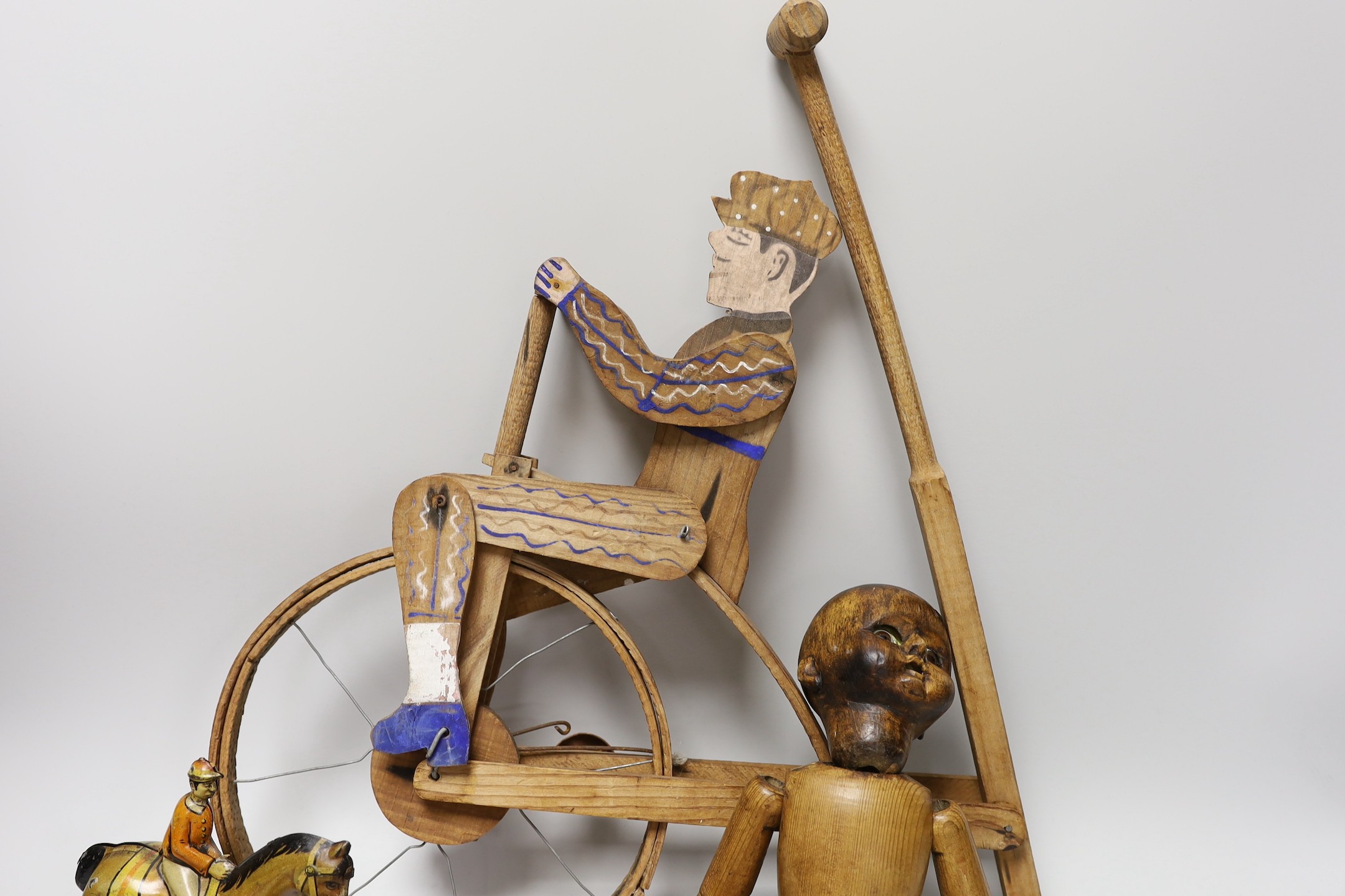 A Victorian carved pine jointed peg doll, jointed wood uni-cyclist toy, two abacuses and an early 20th century German tin plate and clockwork jockey on racehorse